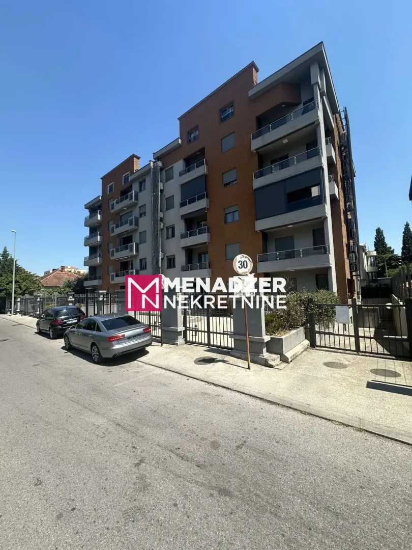 View of the exterior of an apartment building with a street and parked cars.