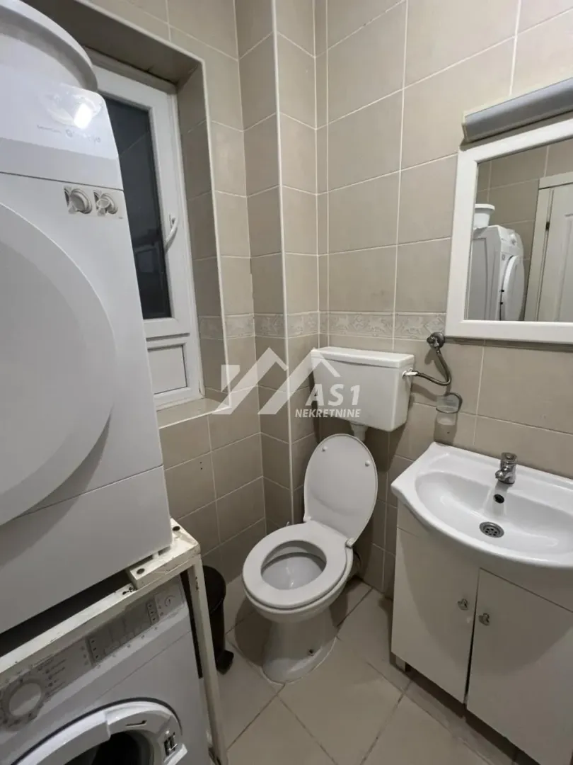 Manje kupatilo sa WC šoljom, umivaonikom, ogledalom i mašinama za pranje veša.
