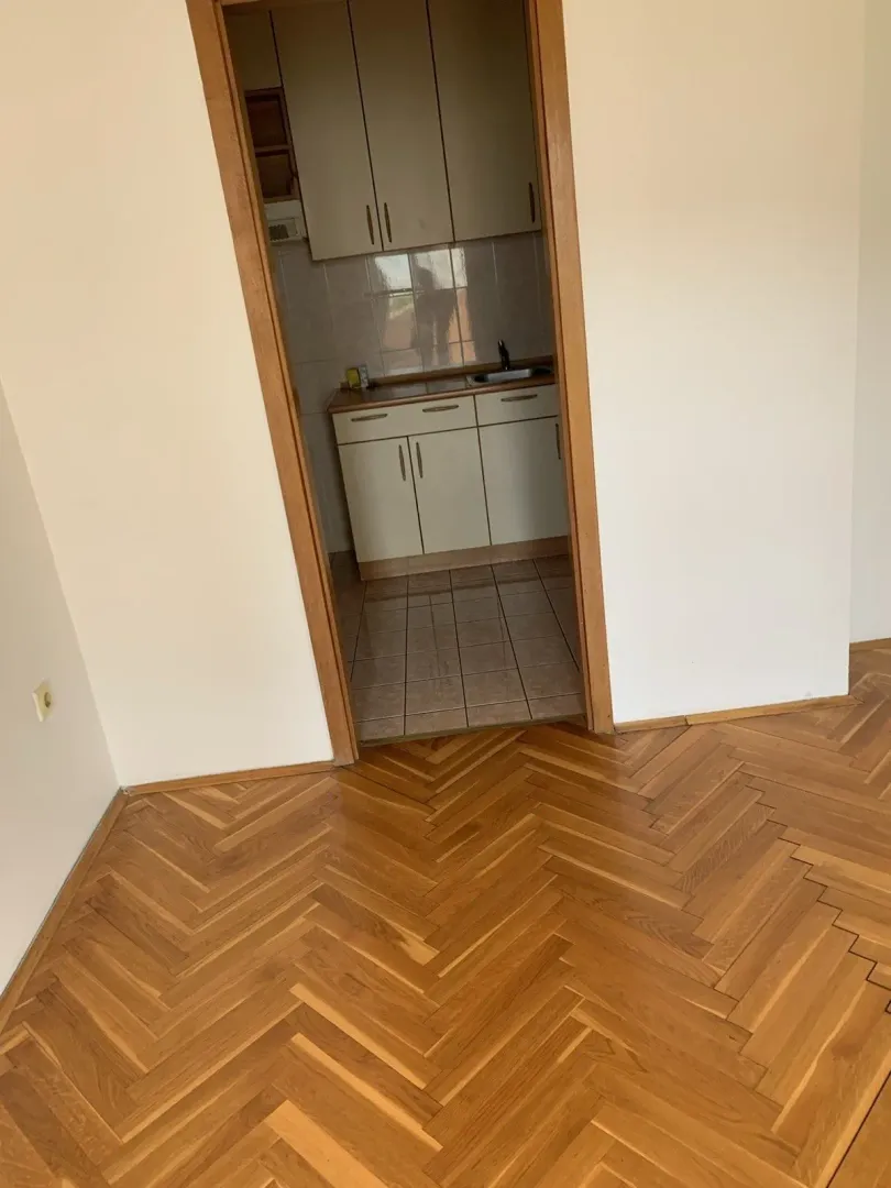 Pogled iz sobe sa parketom na manju kuhinju sa bijelim elementima.