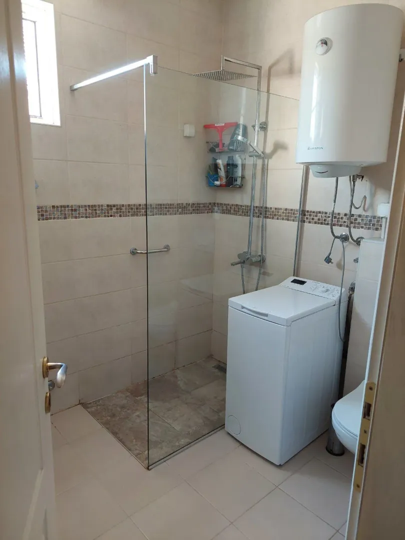 Bright bathroom with a walk-in shower, washing machine, and water heater.
