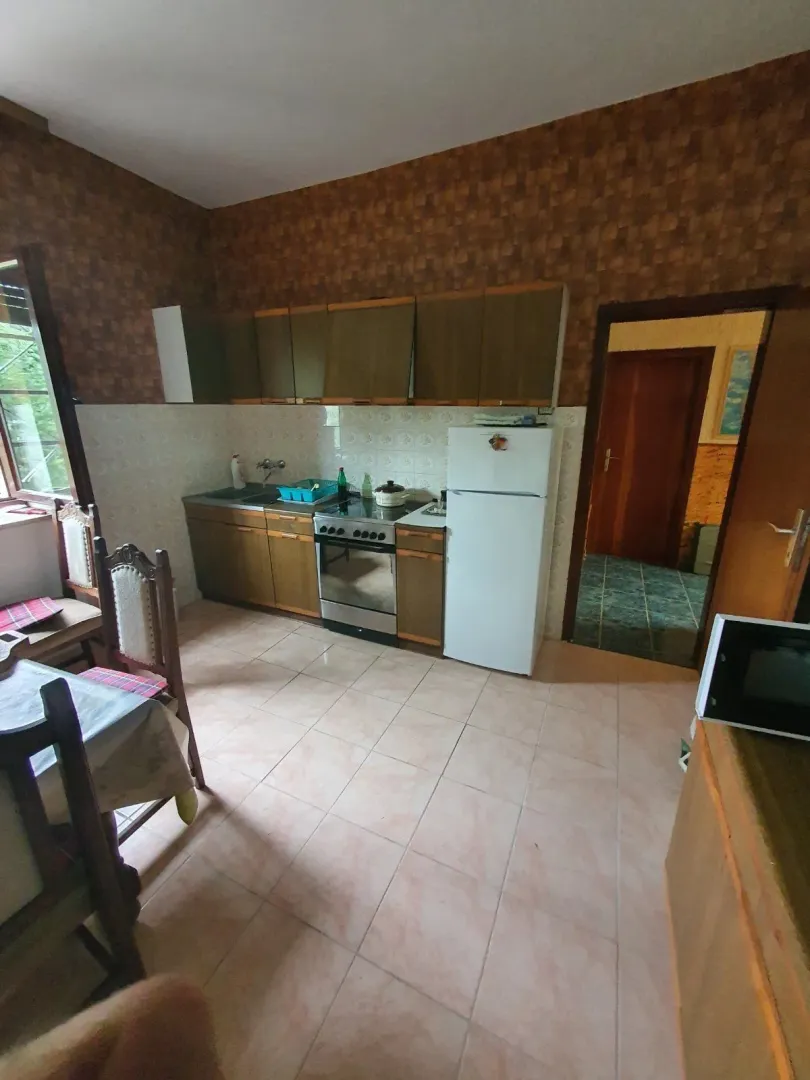 Jednostavna kuhinja sa trpezarijskim stolom i frižiderom.