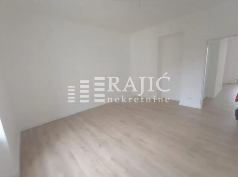 Empty room with light wooden flooring and white walls.