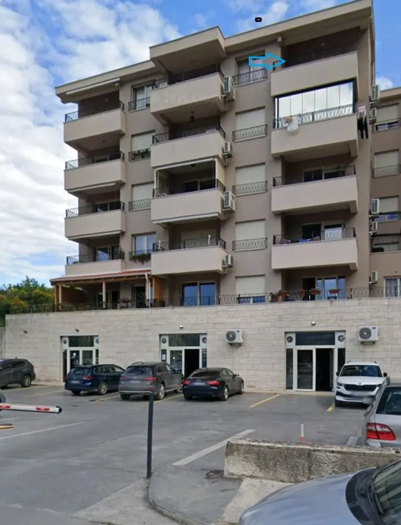 Spoljašnji izgled stambene zgrade sa parkingom ispred.