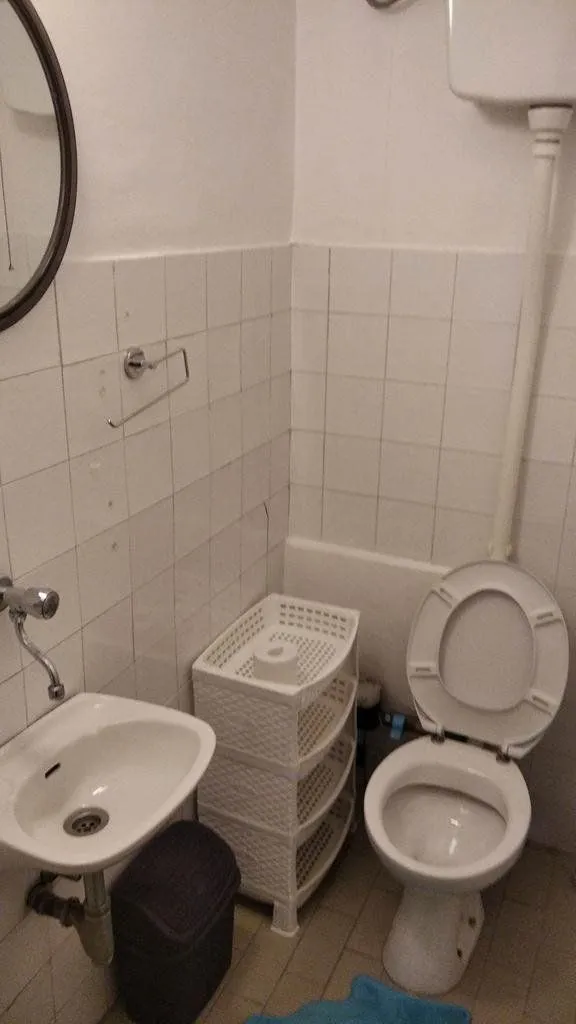 Manje kupatilo sa toaletom, umivaonikom i bijelim zidnim pločicama.
