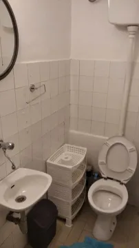 Manje kupatilo sa toaletom, umivaonikom i bijelim zidnim pločicama. - image 3