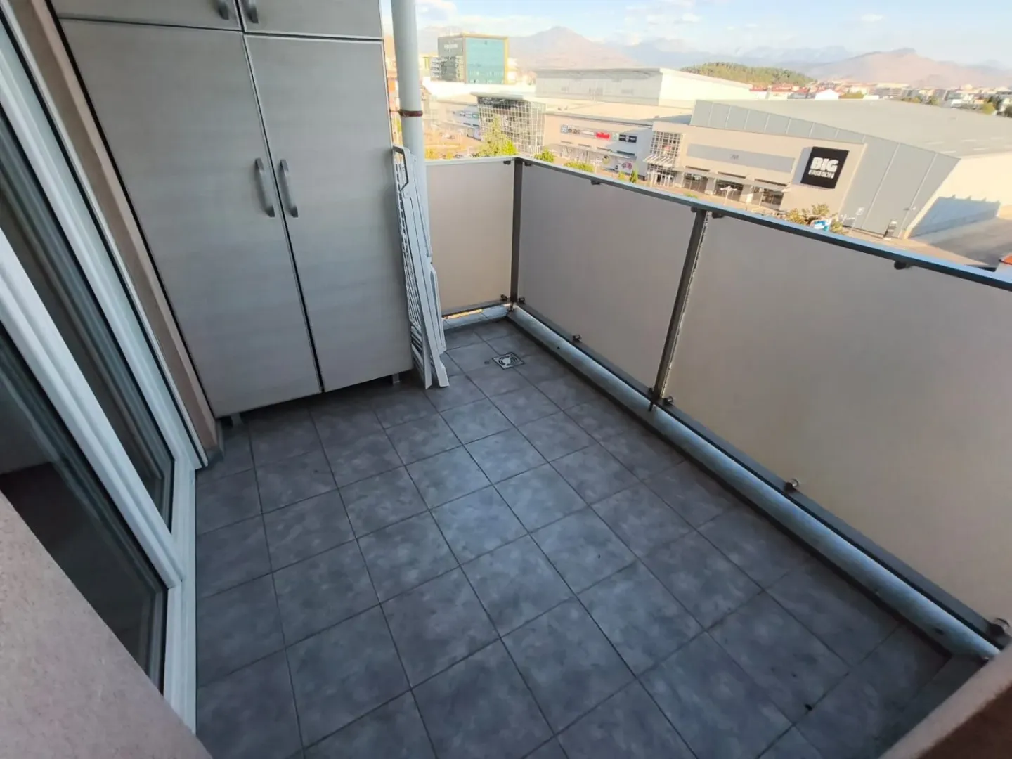 Manji popločani balkon sa ugradnim ormarom i pogledom na okolinu.