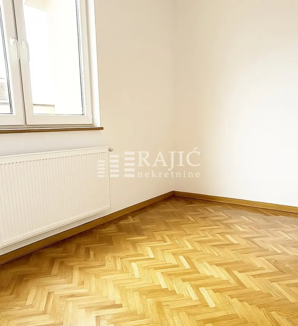 Prazna soba sa parketom i belim zidovima.