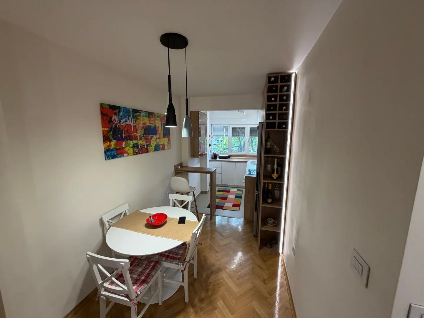 Trpezarija povezana sa kuhinjom sa drvenim podom i modernim osvjetljenjem.