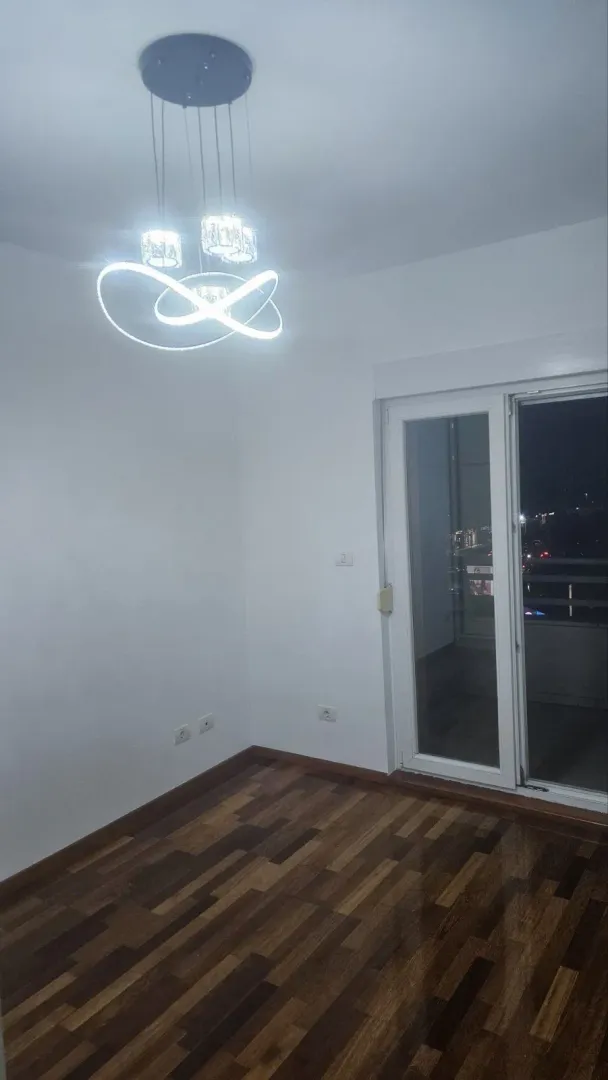 Prazna soba sa modernim lusterom i balkonskim vratima.