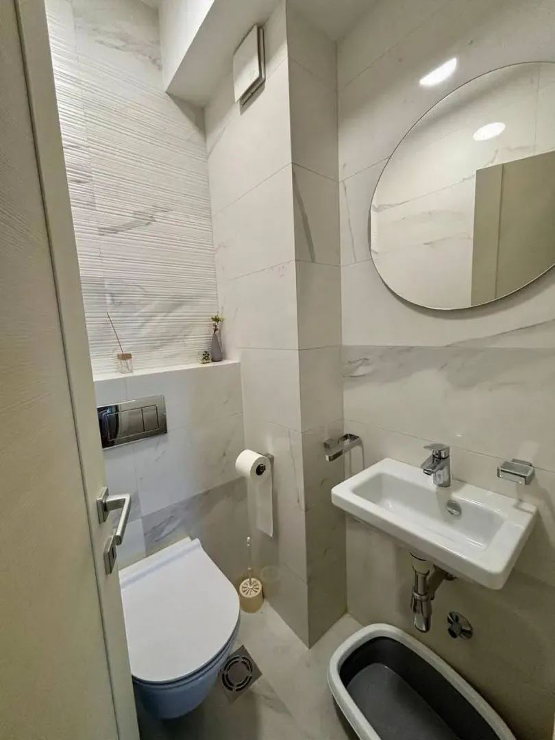 Moderno opremljeno kupatilo sa bijelim pločicama, umivaonikom i toaletom.