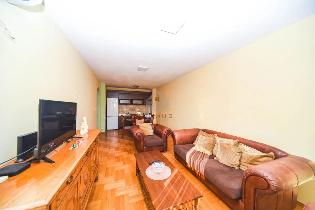 Living room with a sofa, TV cabinet, and dining area in the background.