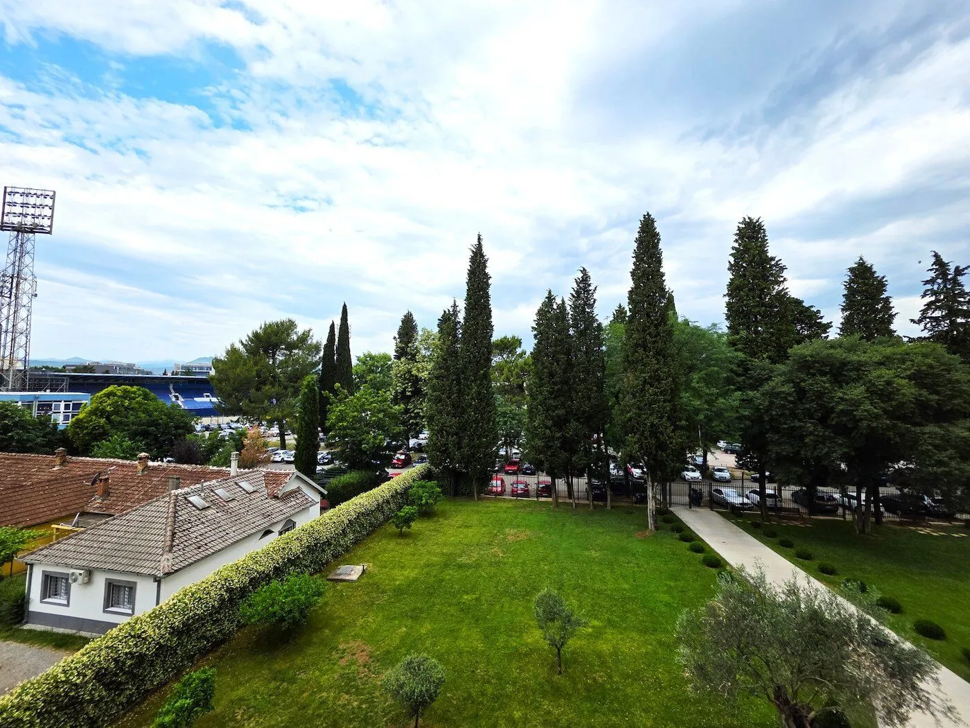 Pogled sa terase na uređeno dvorište sa zelenilom i okolne objekte.