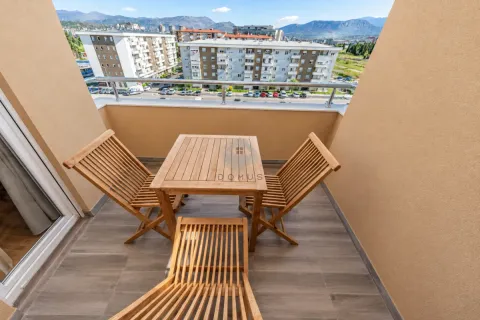 Small furnished balcony with a wooden table, chairs and city view. - image 28