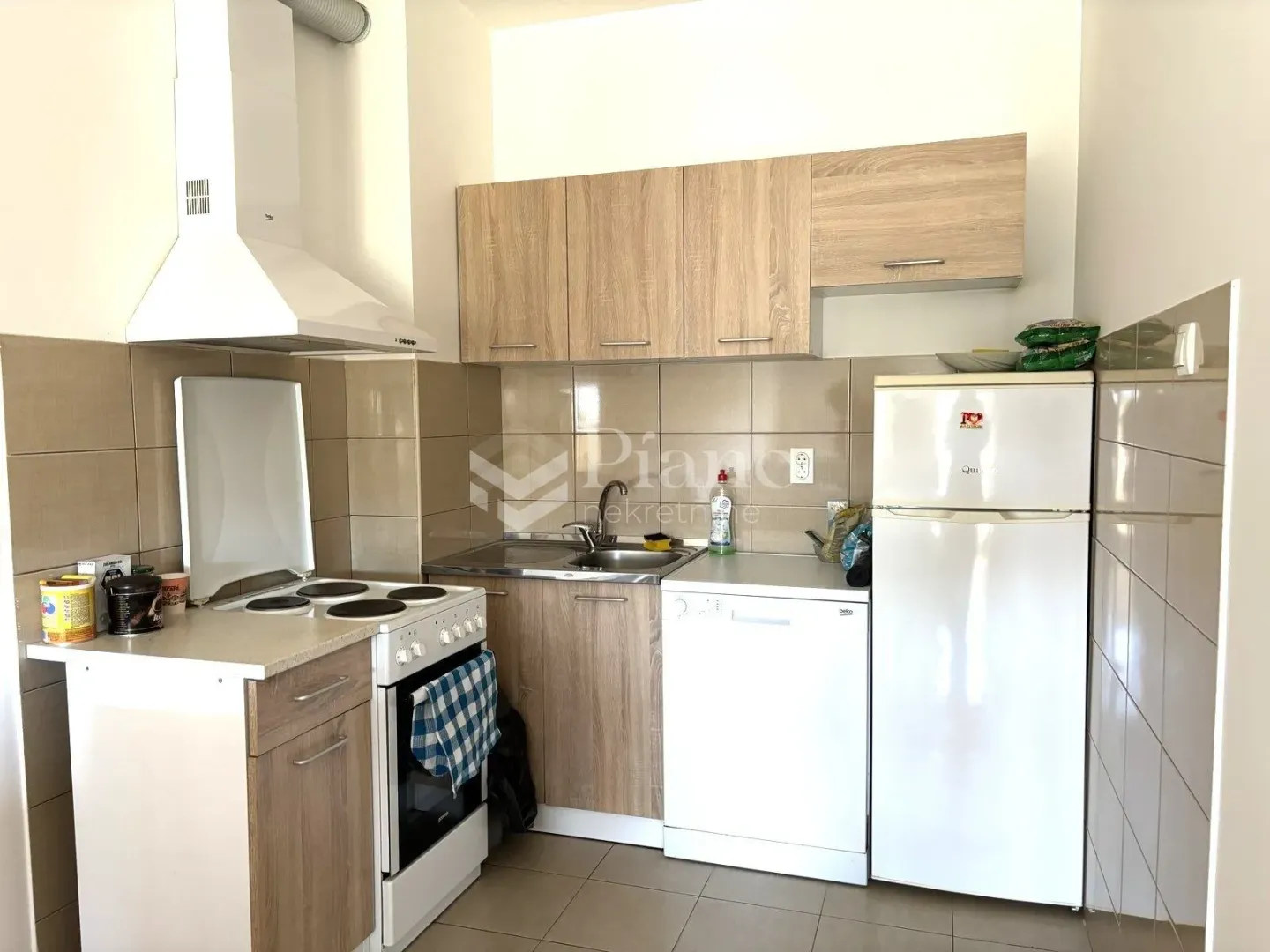 Smaller kitchen with wooden units, stove, refrigerator and sink.