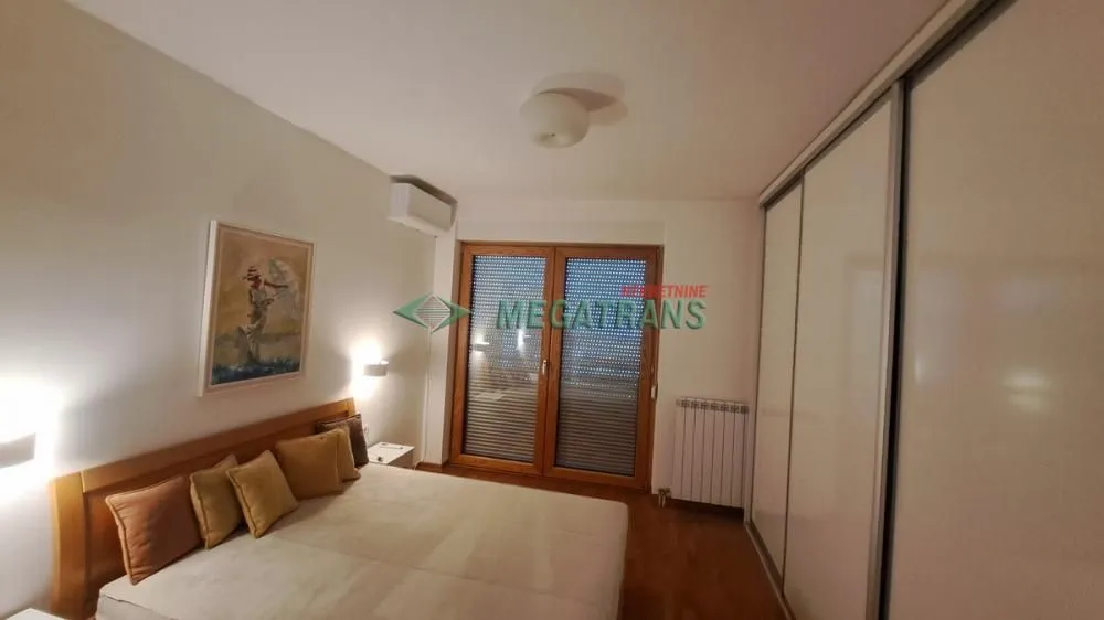 Nameštena spavaća soba sa bračnim krevetom, velikim plakarom i izlazom na terasu.