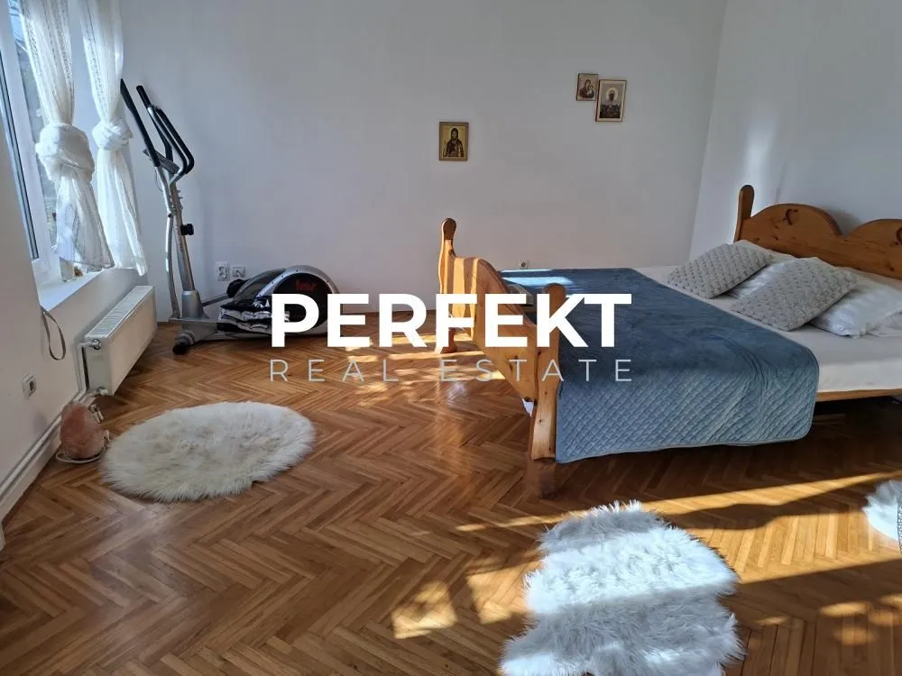 Spavaća soba sa bračnim krevetom, drvenim parketom i trenažerom.