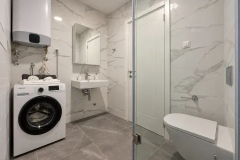 Modern bathroom with white marble tiles, toilet, sink and washing machine. - image 7
