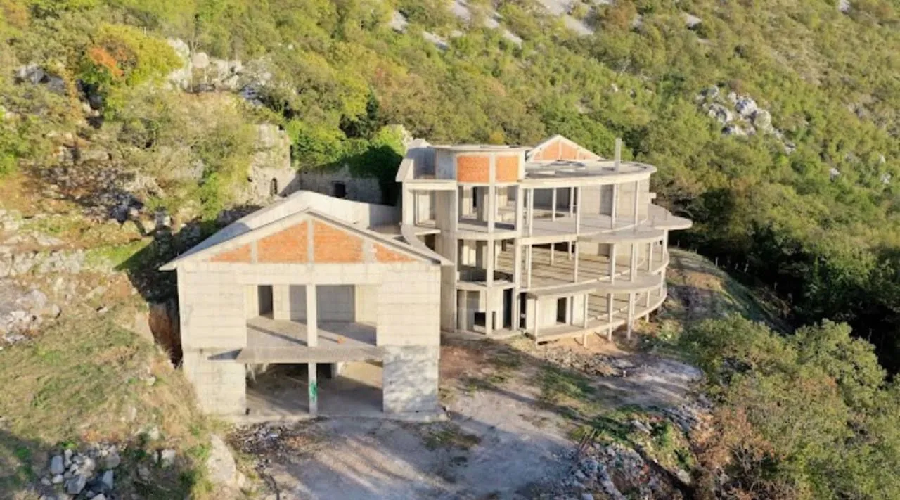 Pogled iz vazduha na nedovršenu kuću u izgradnji okruženu prirodom.