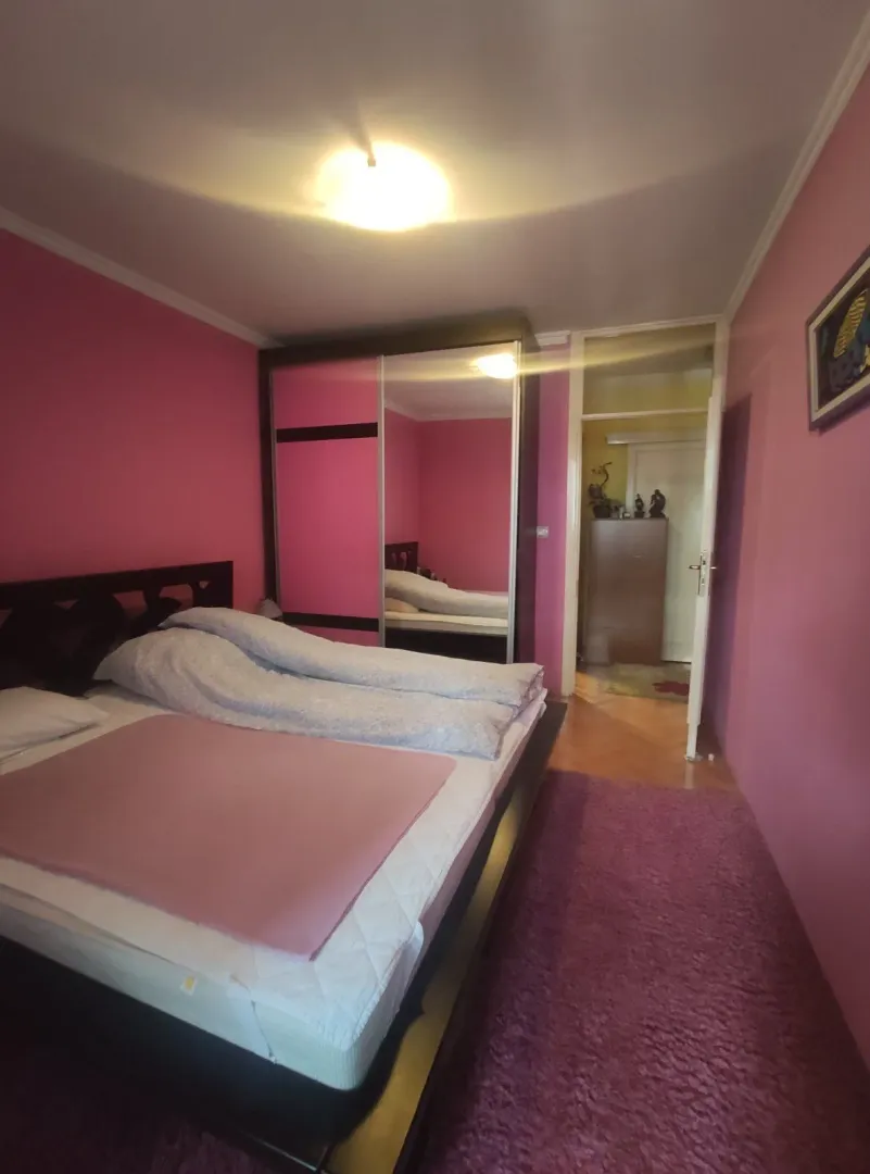 A bedroom featuring pink walls, a large bed, and a mirrored wardrobe.