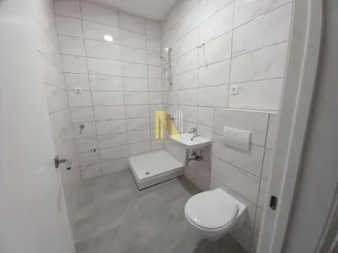 Manje kupatilo sa tuš kabinom, umivaonikom i WC šoljom obloženo svetlim pločicama. - image 10