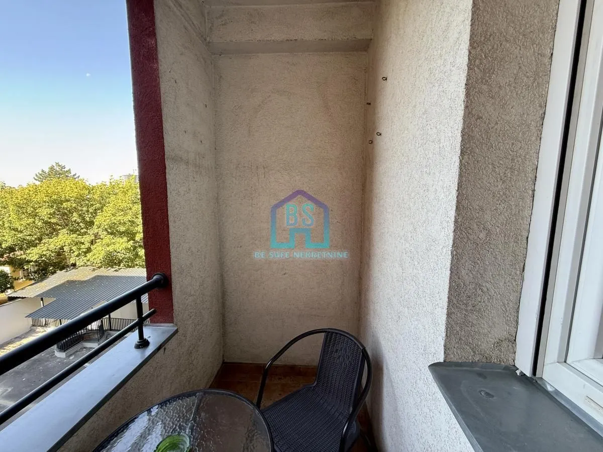 Manji natkriveni balkon sa stolom i jednom stolicom i pogledom na zelenilo.