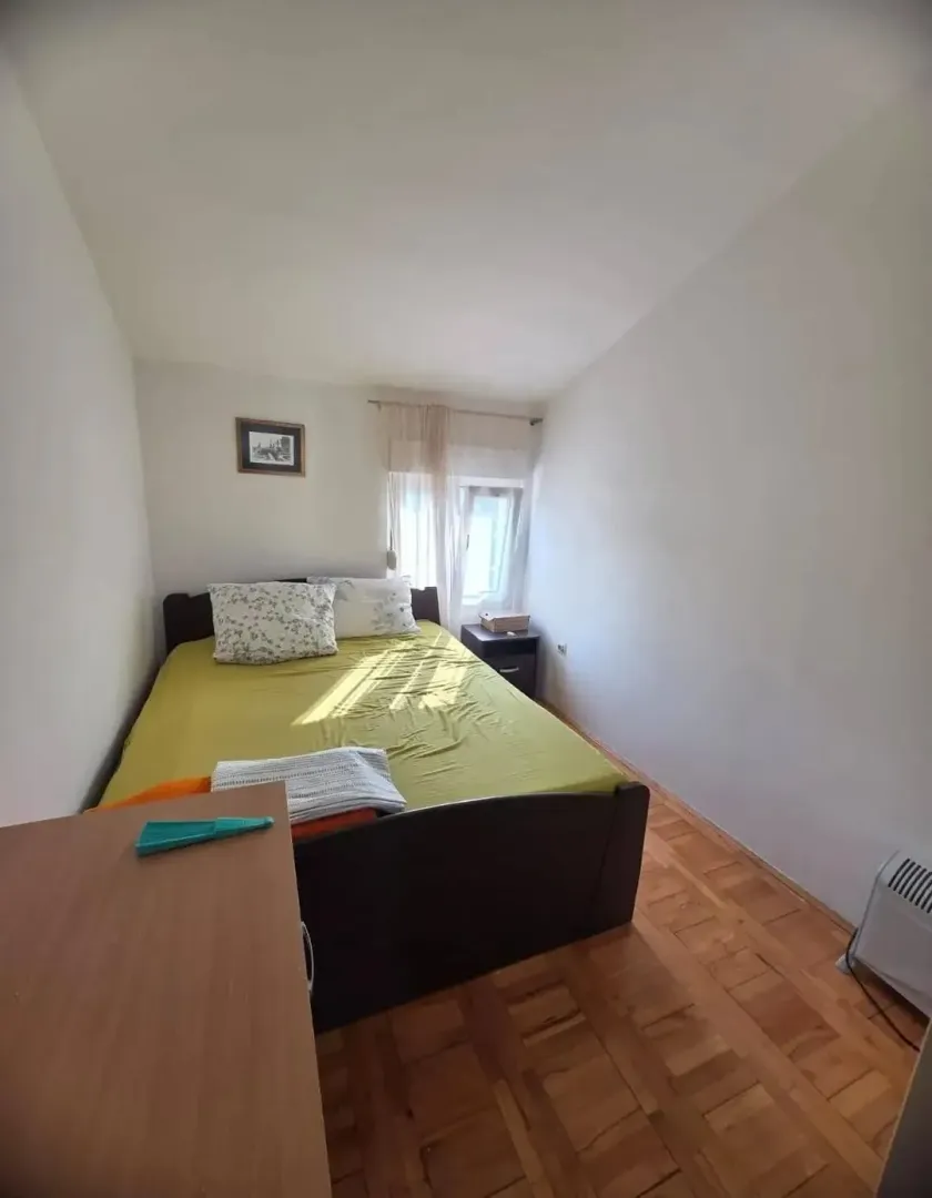 Spavaća soba sa bračnim krevetom, prozorom i drvenim podom.