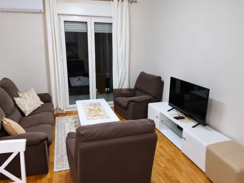 Dnevna soba sa garniturom za sjedenje, TV komodom i balkonskim vratima. - image 2