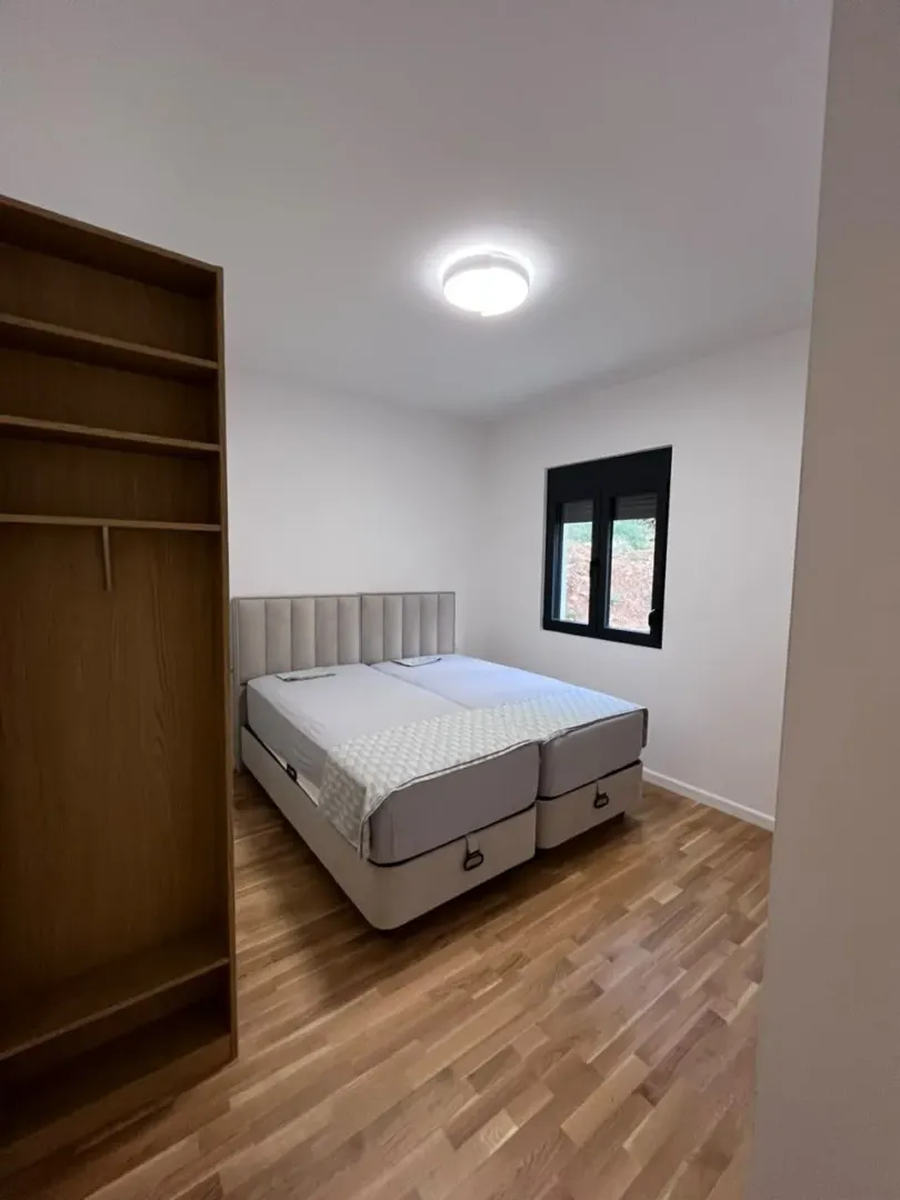 Spavaća soba sa bračnim krevetom, drvenim podom i garderoberom.