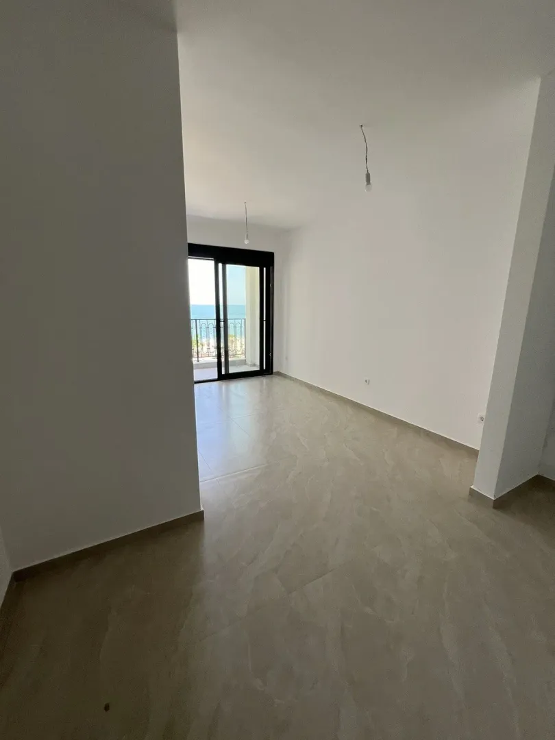 An empty and bright room with balcony access offering a view of the sea.