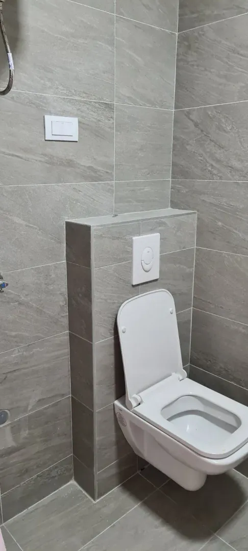 Kupatilo sa sivim pločicama i ugradnim toaletom.