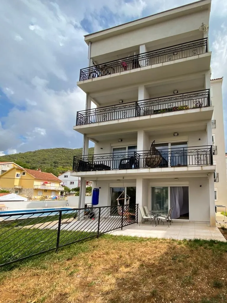 Exterior view of a three-story residential building with terraces and a swimming pool in the yard.
