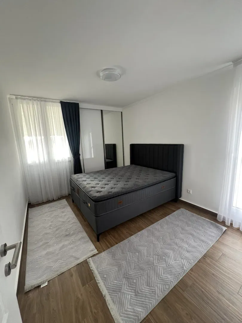 Bright bedroom featuring a double bed, a mirrored wardrobe, and two grey rugs.