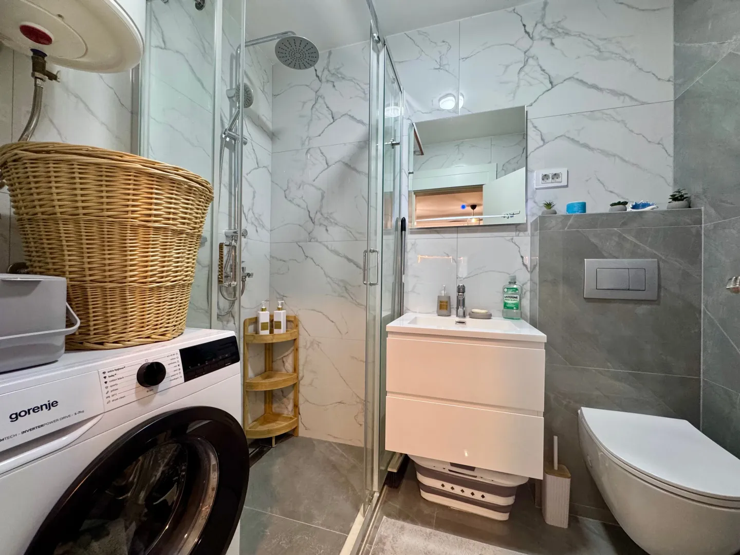 Modernly equipped bathroom with a shower cabin, vanity, and washing machine.