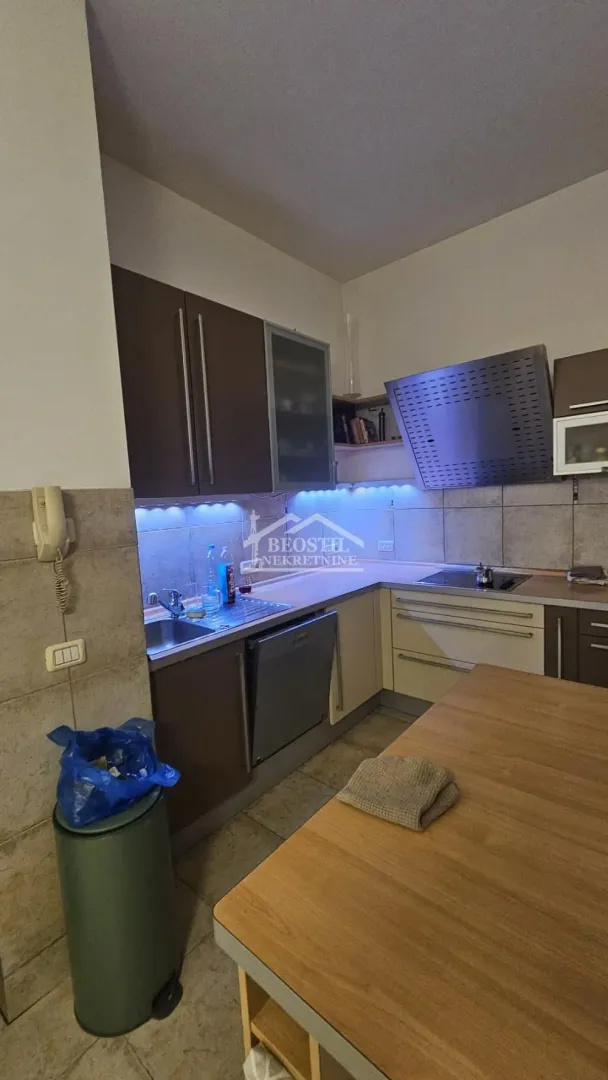 Kuhinja sa braon elementima, sudoperom, radnom površinom i ugradnom pločom.