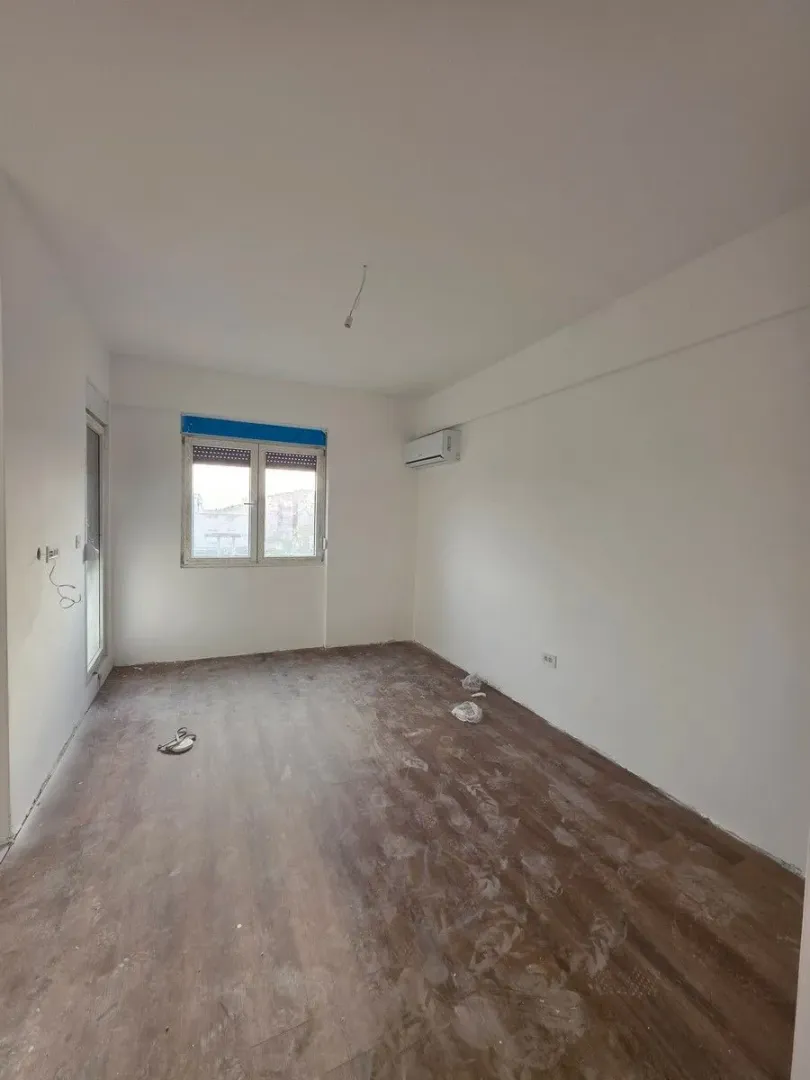 Prazna soba sa bijelim zidovima, klima uređajem i prozorom.