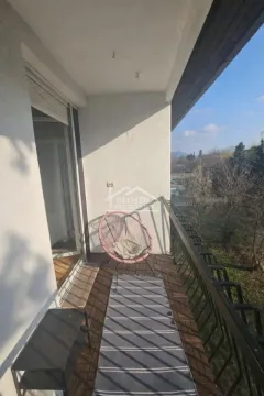 Covered balcony with wooden flooring, a chair, and a view of greenery. - image 2