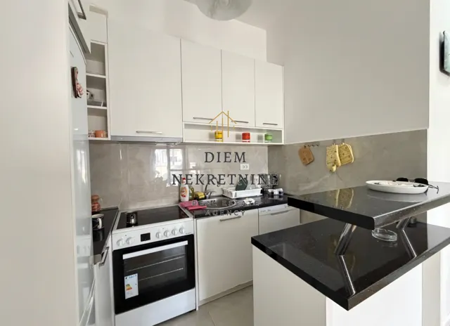 Moderna bijela kuhinja sa crnim radnim površinama i šankom.