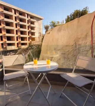 Terrace with a table, chairs, and glasses of juice overlooking a neighboring building under construction. - image 9