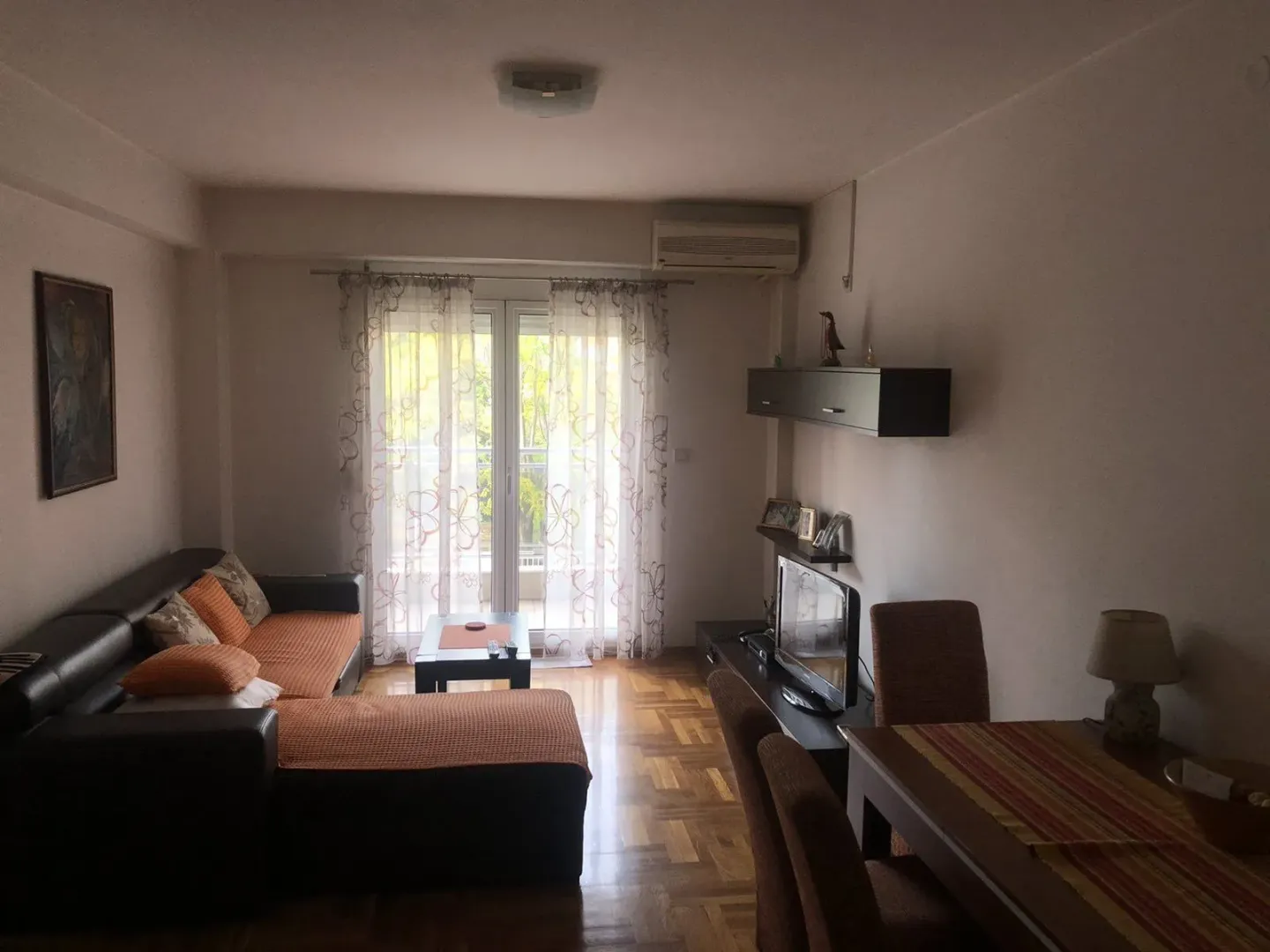 Dnevna soba sa ugaonom garniturom, trpezarijskim stolom i balkonskim vratima.