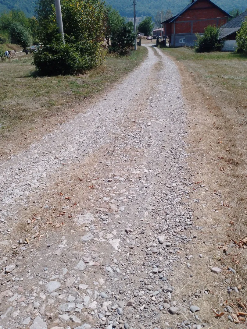 Prikaz makadamskog puta koji vodi prema imanju sa kućom u pozadini.