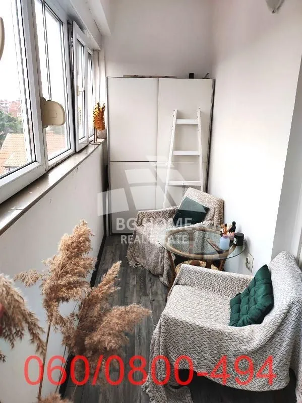 Zastakljeni balkon sa garniturom za sedenje i ormarom.