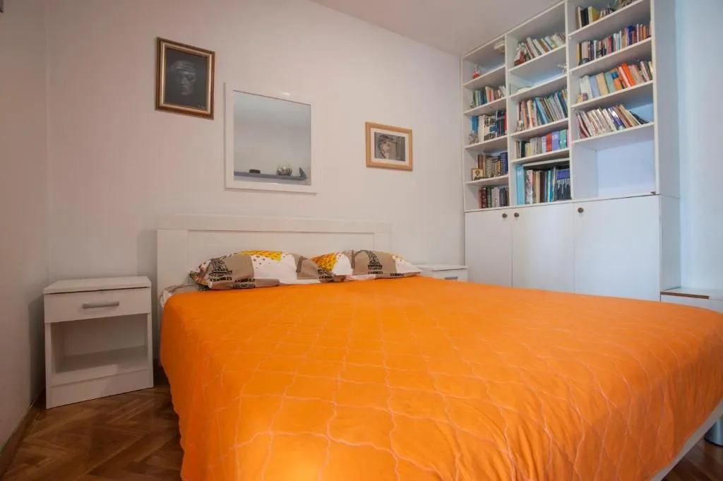 A bedroom with a double bed, a white bedside table, and a built-in bookcase.
