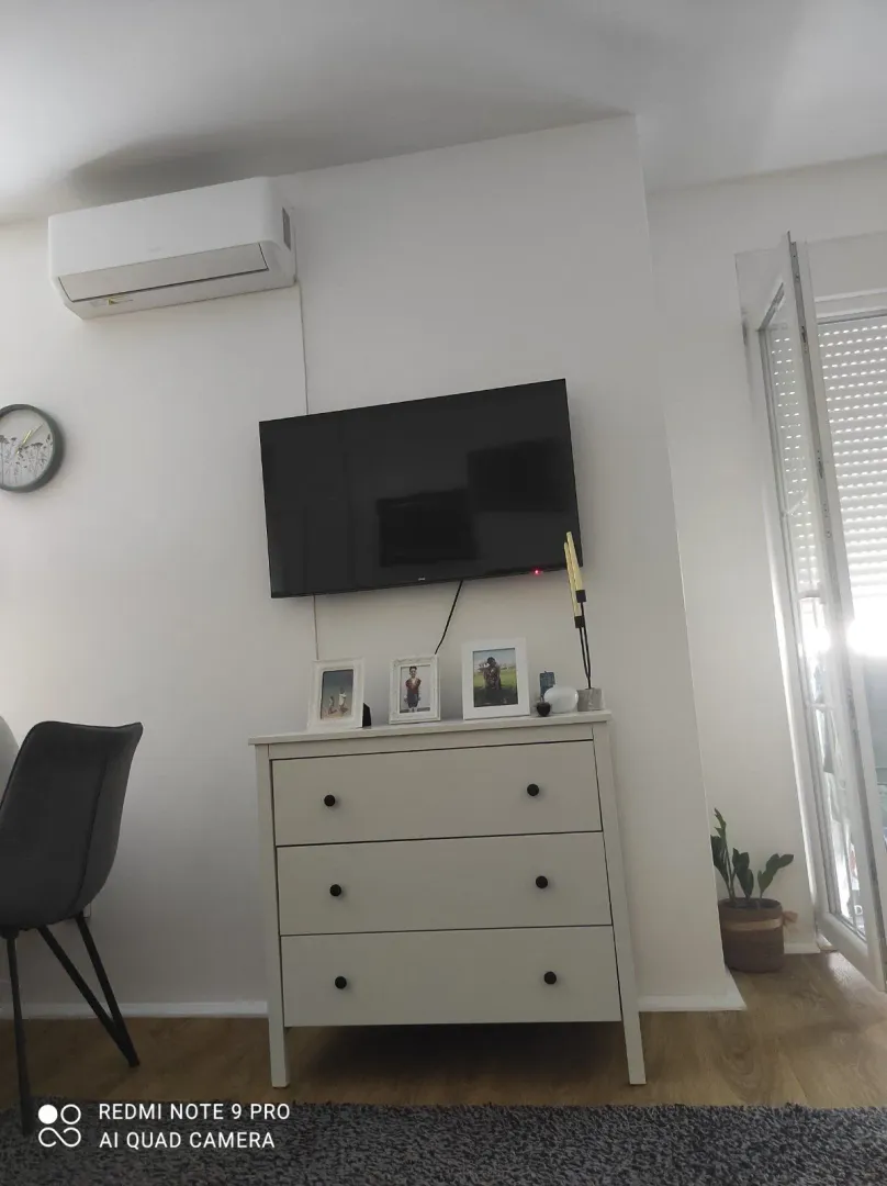 Living room with a chest of drawers, television, and air conditioning unit.
