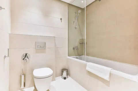 Kupatilo opremljeno WC šoljom, kadom sa staklenom pregradom i bež pločicama. - image 17
