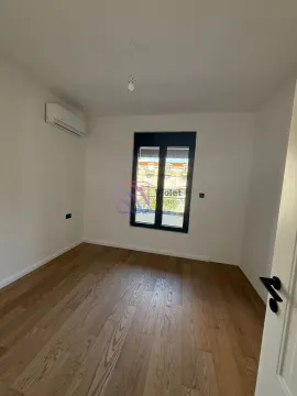 Prazna soba sa bijelim zidovima, drvenim podom, klima uređajem i prozorom. - image 7