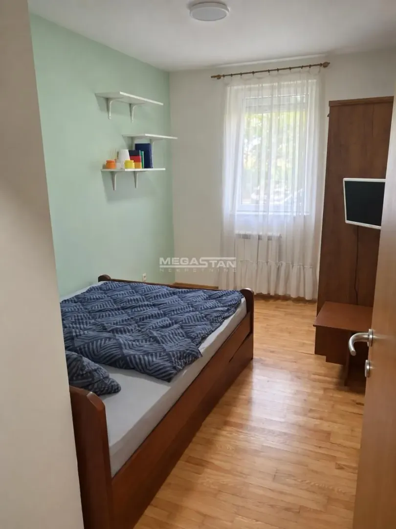 Manja spavaća soba sa krevetom, drvenim ormanom i prozorom.