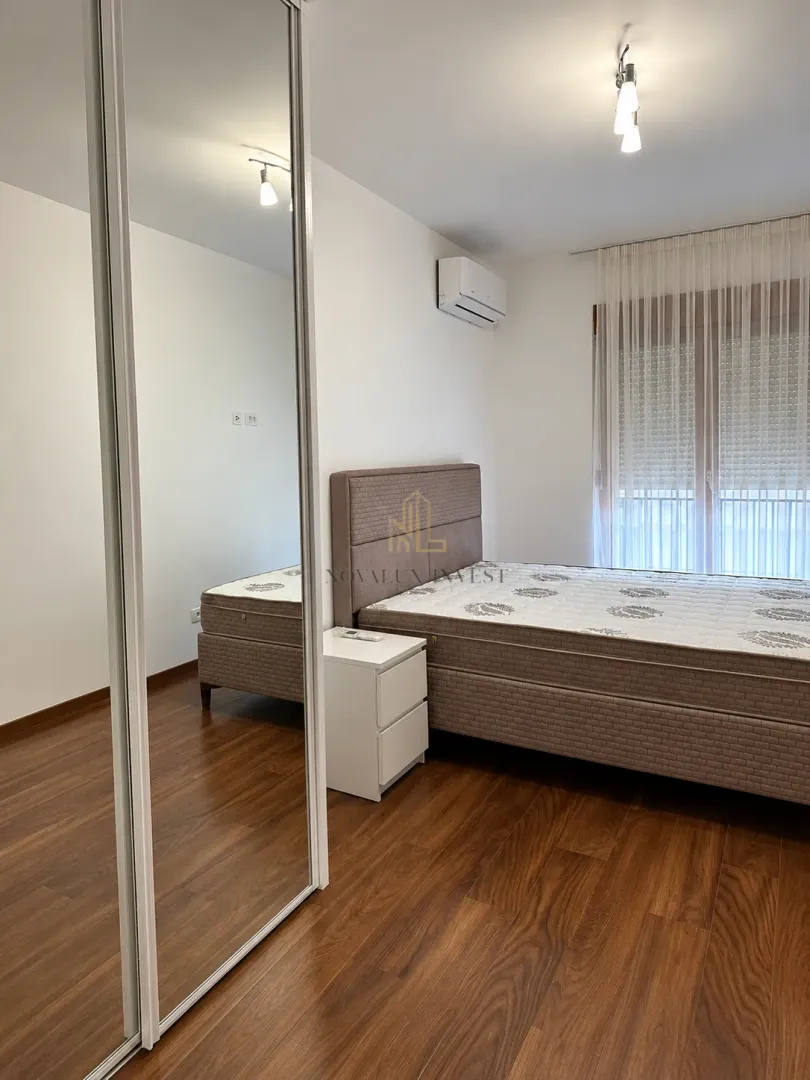 Spavaća soba sa bračnim krevetom, noćnim stočićem i velikim ogledalom na ormaru.