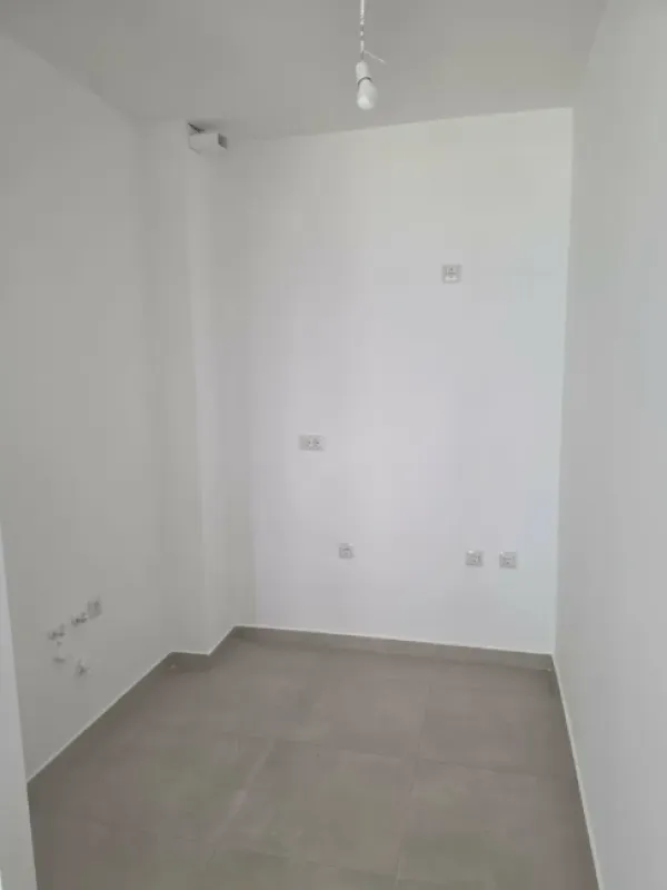 Prazna neopremljena prostorija sa bijelim zidovima i sijalicom na plafonu.