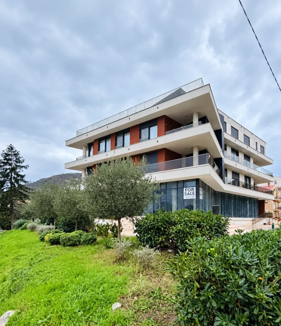 Exterior of a modern residential building with a landscaped yard and a for sale sign.