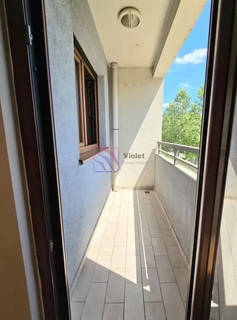 Dugačak popločani balkon sa metalnom ogradom i pogledom na zelenilo.